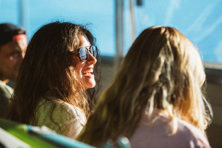 Two women are sitting on a bus, sunlight shining on them.