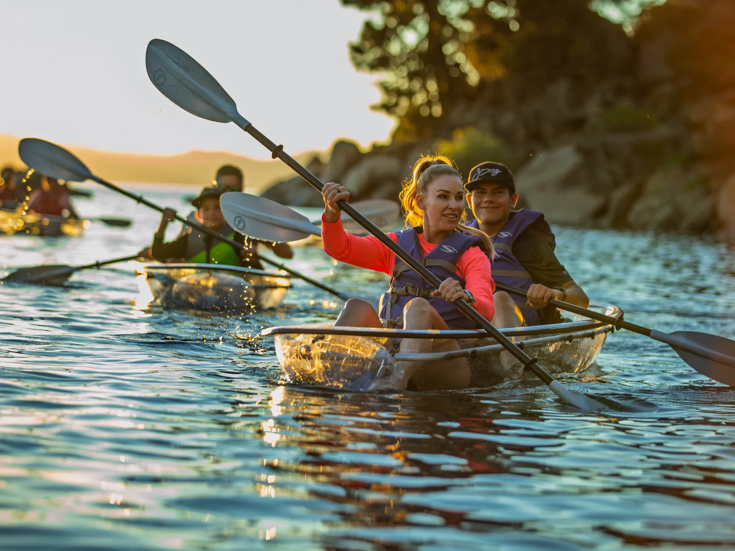 People kayaking in transparent kayaks on a sunny lake.