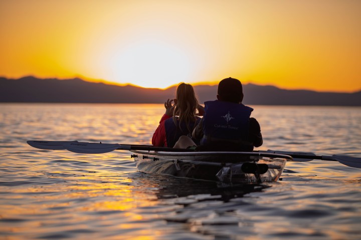 Two people kayaking on a lake at sunset with mountains in the distance.
