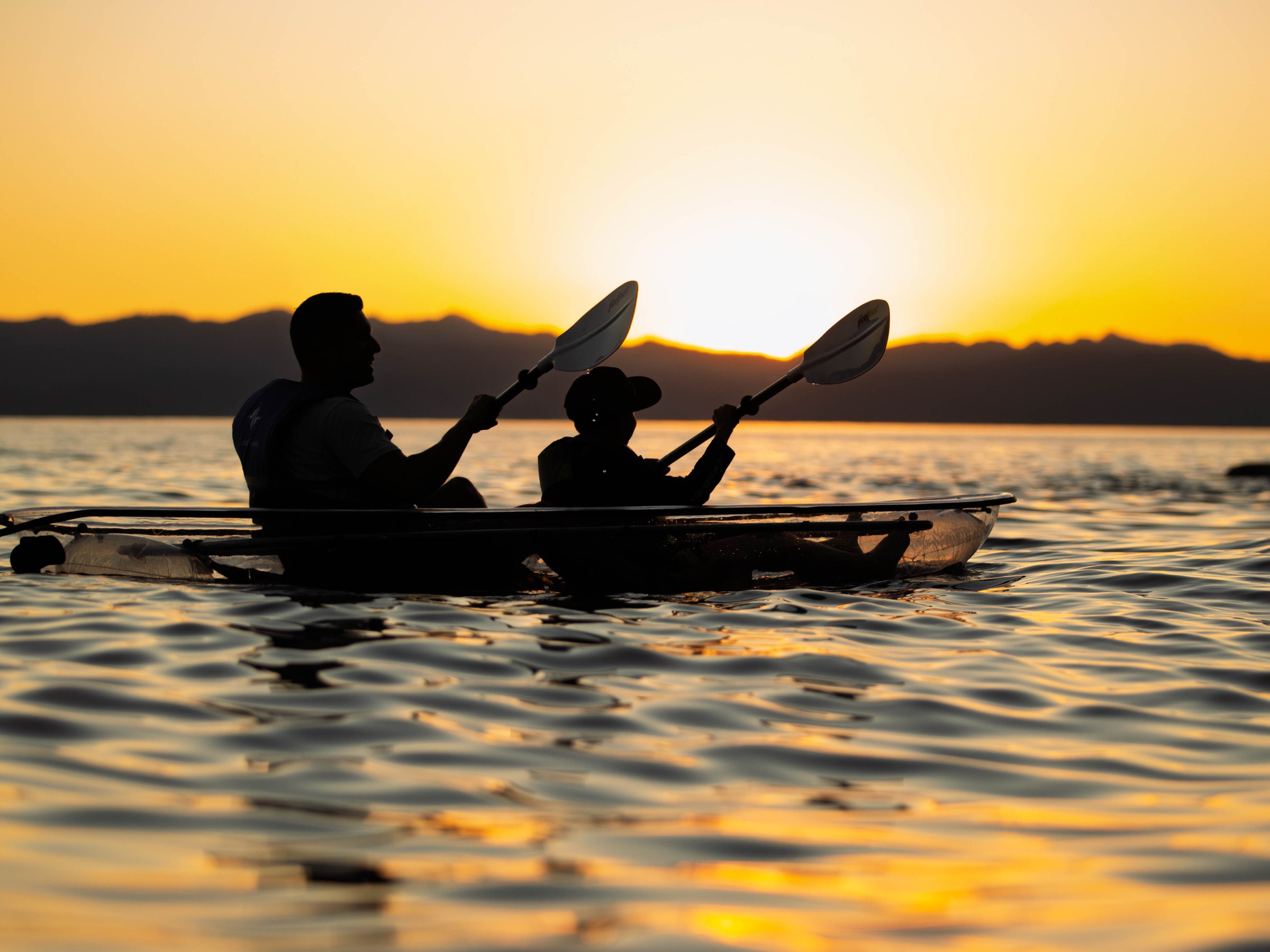 Silhouetted kayakers at sunset on a calm lake.