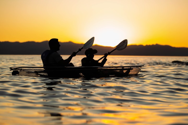Silhouetted kayakers at sunset on a calm lake.