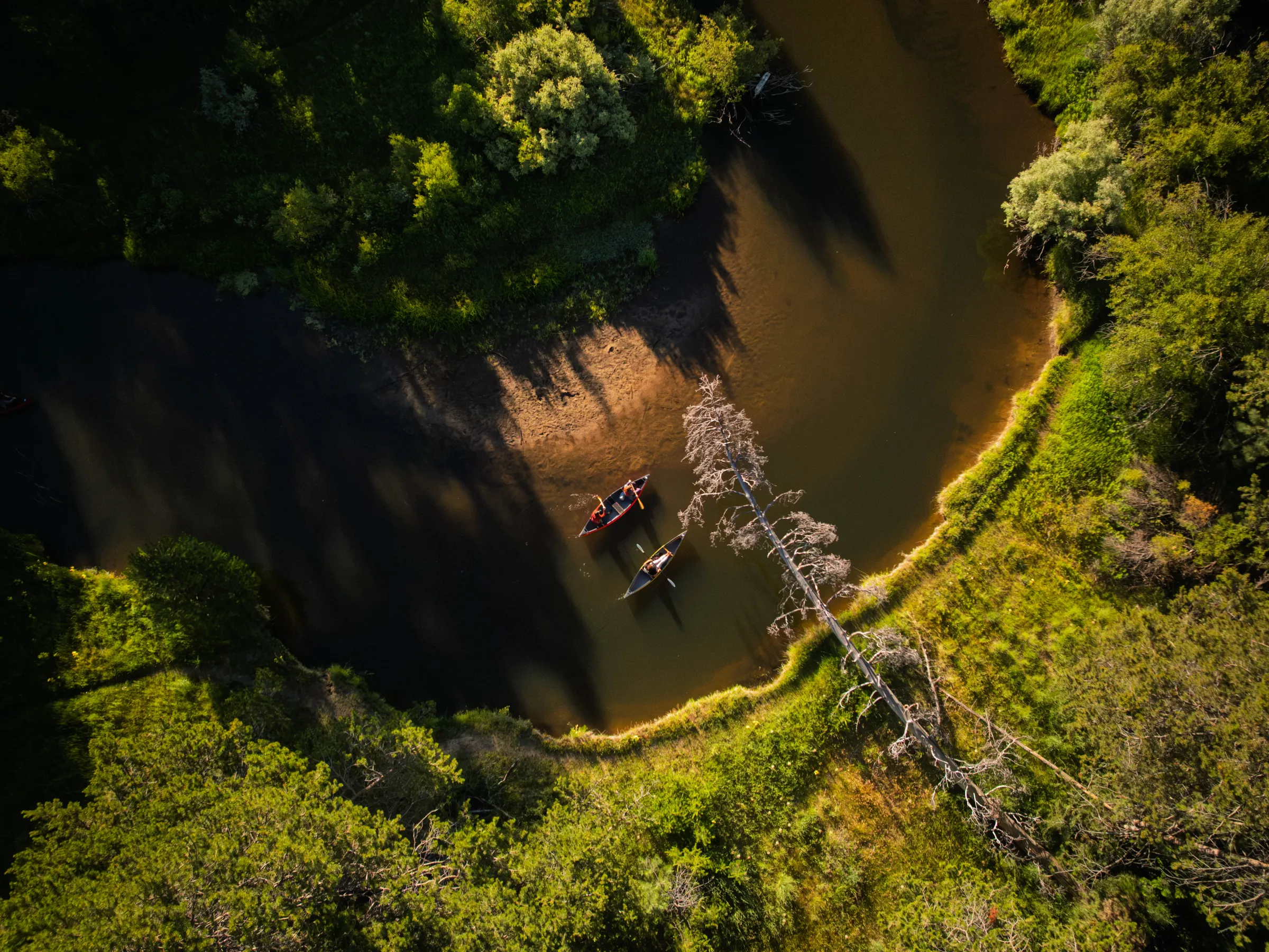 Aerial view of two canoes on a winding river surrounded by lush, green forest.