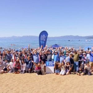 Group of people posing on a sunny beach with mountains in the background.