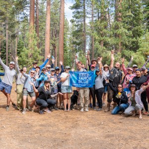 Group of people outdoors holding a 'Keep Tahoe Blue' sign, surrounded by trees.