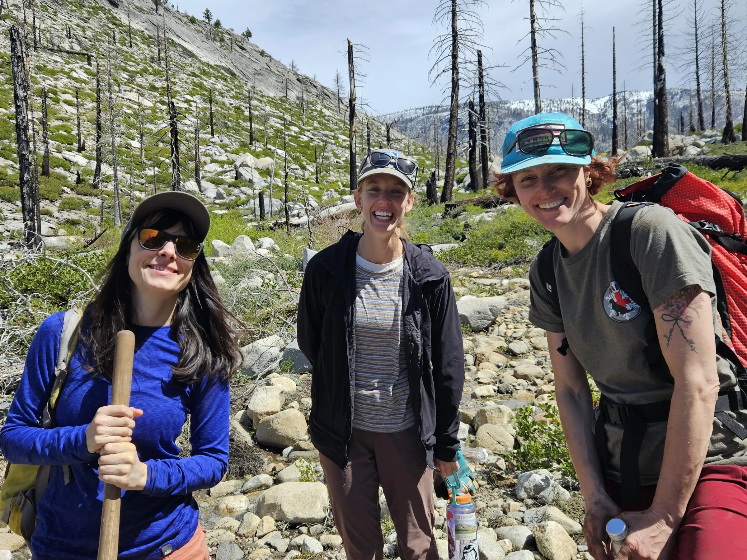 Three people hiking on a rocky trail with bare trees in the background.