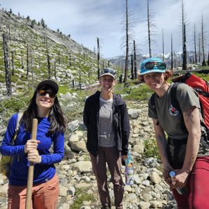 Three people hiking on a rocky trail with bare trees in the background.