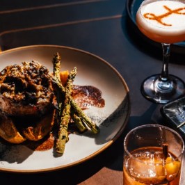 Elegant dish with meat and asparagus, cocktail, dessert on a table.