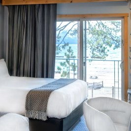 Hotel room with two beds, fireplace, and a view of a lake through a sliding glass door.