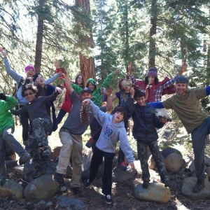 Group of people hiking in a forest, posing energetically with trees in the background.