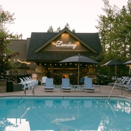 Outdoor pool with lounge chairs and string lights next to a cabin.