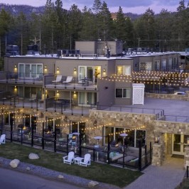 A modern lodge with string lights in a forested area at dusk.