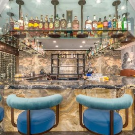 Upscale bar with blue stools, marble counter, and illuminated shelves of bottles.