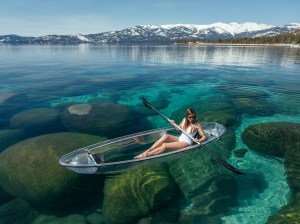 Woman kayaking in clear water with mountains in the background.