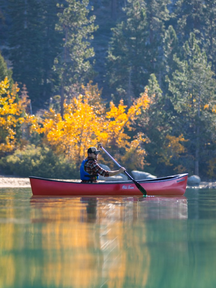 Person canoeing on a calm lake with autumn trees in the background.